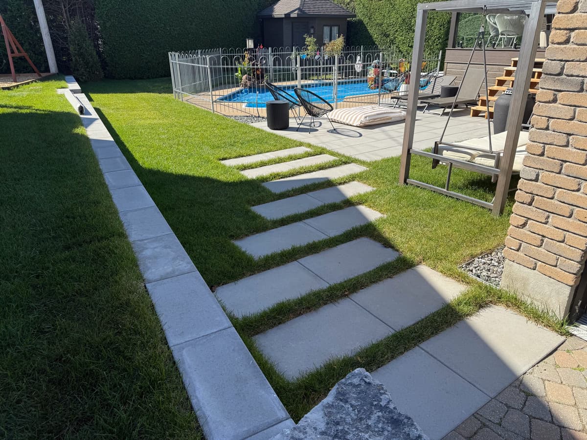 Après les travaux — cour arrière aménagée avec allée piétonne en grandes dalles de béton, bordures et gazon autour de la terrasse et de la piscine