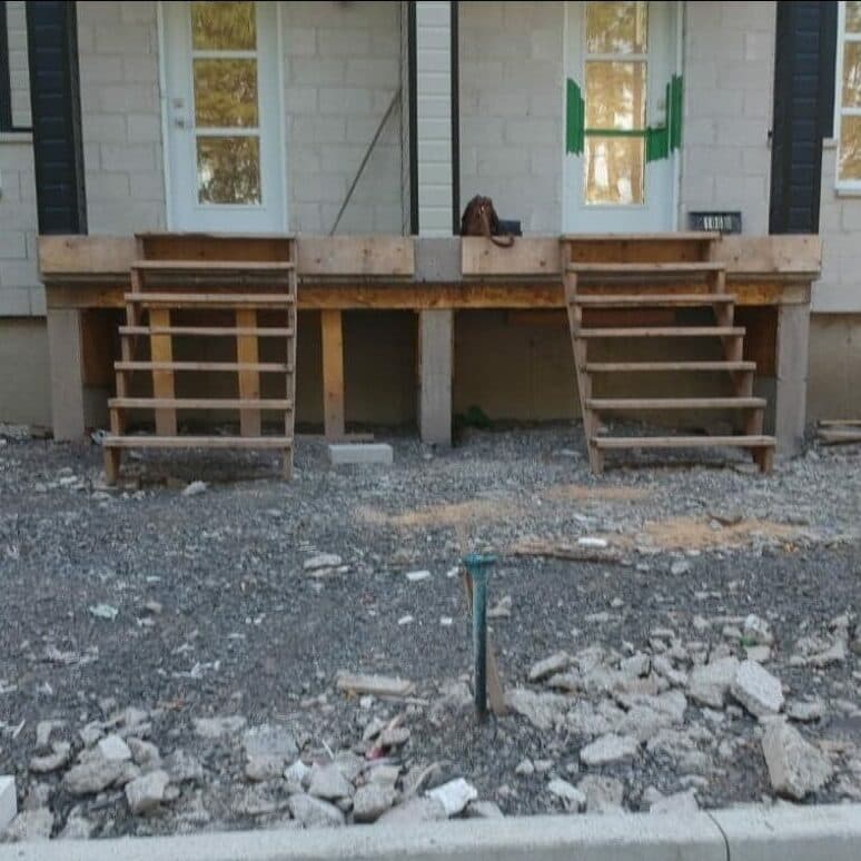 Avant les travaux — façade de duplex avec escaliers temporaires et terrain de gravier