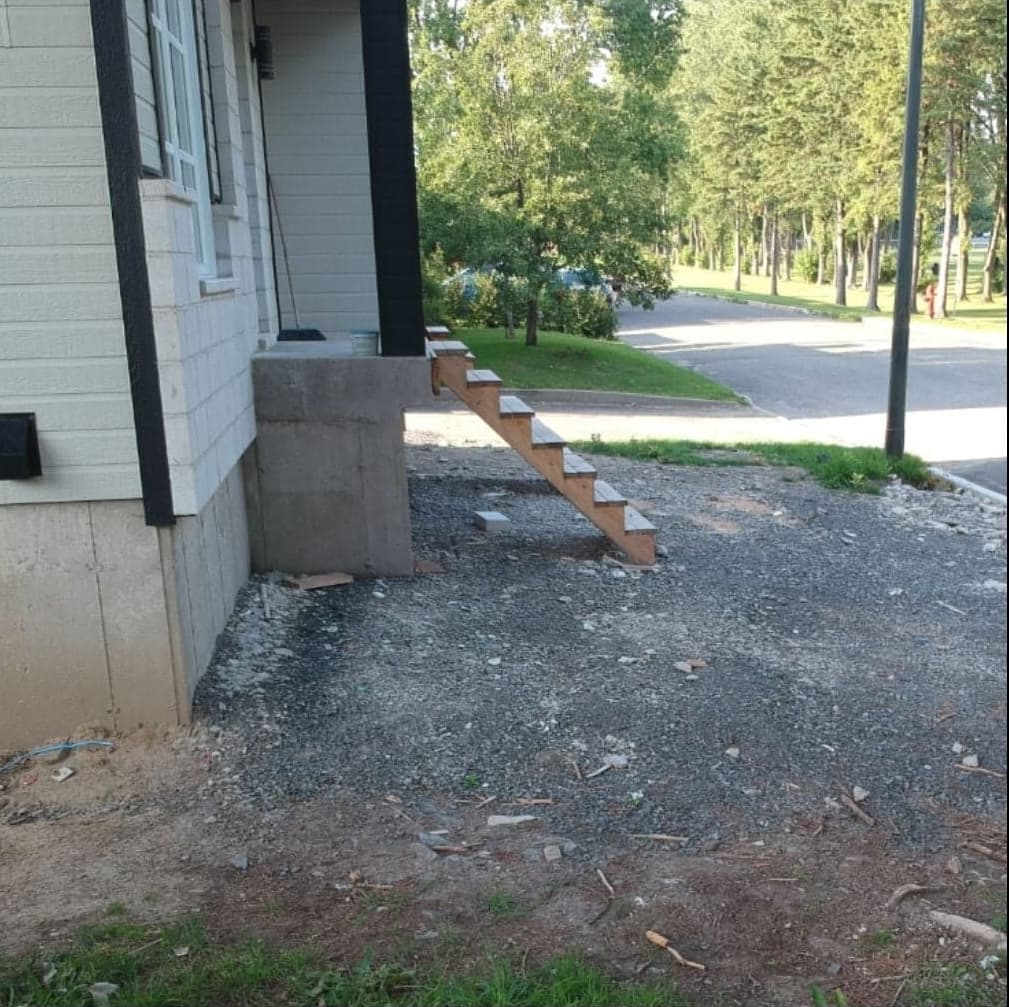 Avant les travaux — terrain en gravier sous un escalier temporaire devant une maison
