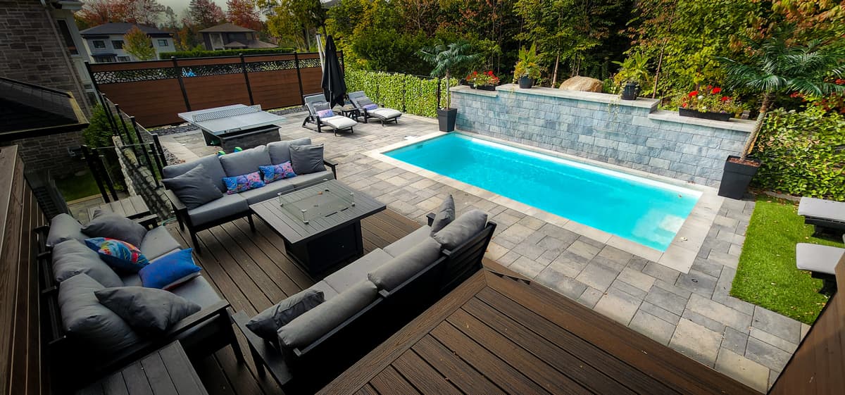 Après les travaux — cour arrière aménagée avec piscine creusée, pavé uni, muret de pierre et espace terrasse avec mobilier extérieur